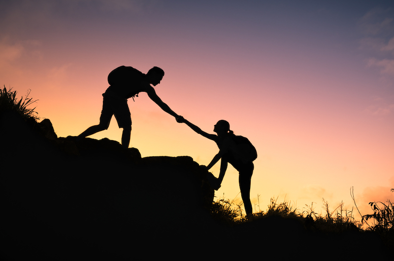 People helping each other hike up a mountain at sunrise