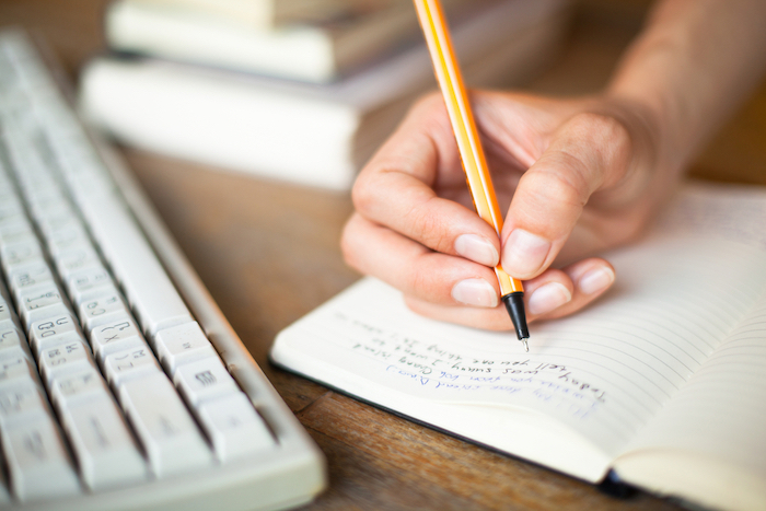 hand writing notes in notebook next to books