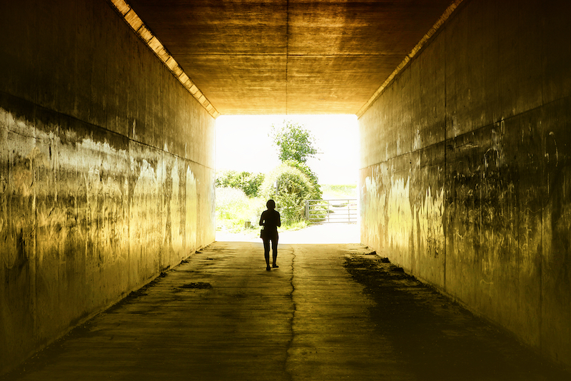 person walking through dark tunnel to sunlight