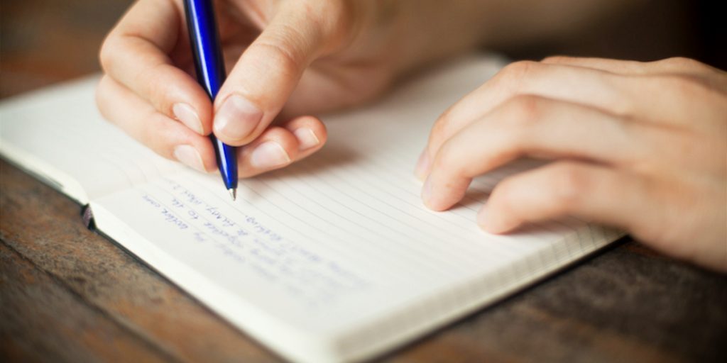 Image of hands writing with a pen in an open journal