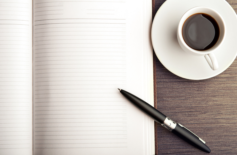 Open a blank white notebook, pen and cup of coffee on the desk