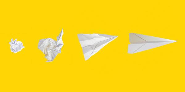 white paper airplanes, from crumpled to smooth, on yellow background