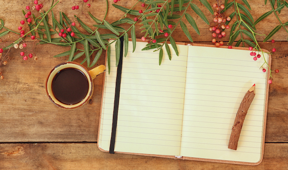 Open journal, with cup of coffee, rustic pencil, and greenery