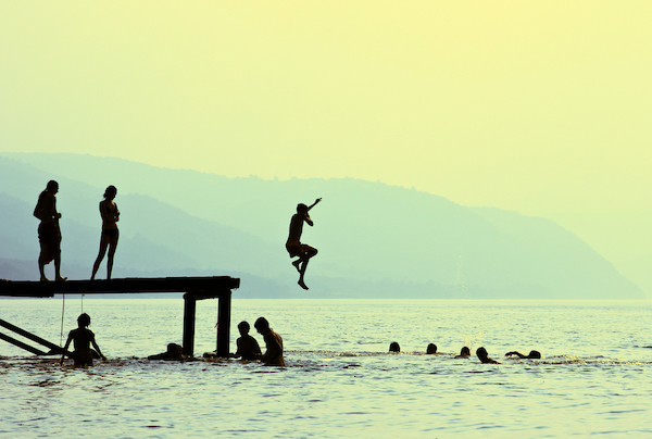 Silhouettes of kids who jump off dock on the lake at sunset.