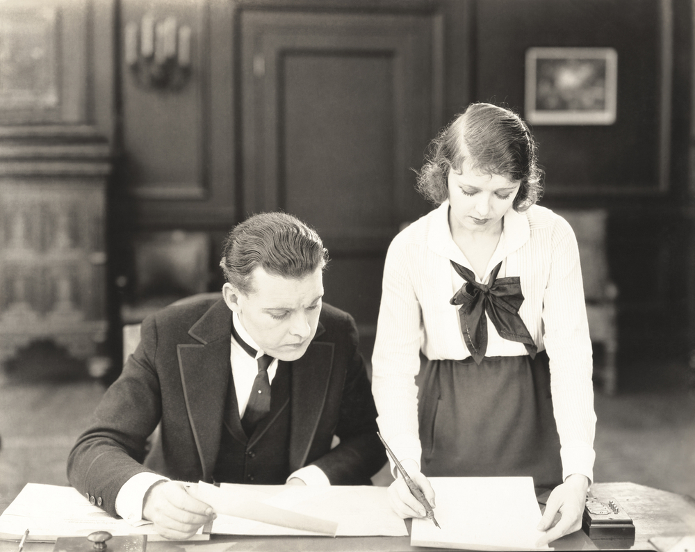 Black/white photo of man and woman working together on papers in an office, early 20th century