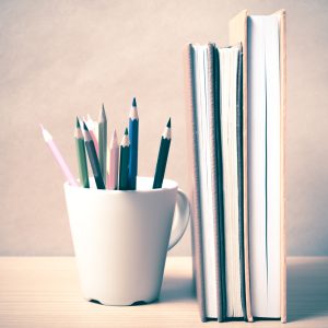 Books standing up next to a jar of color pencils